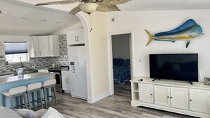 Une cuisine moderne avec des armoires blanches, un îlot central doté de tabourets de bar, un ventilateur de plafond et une fresque représentant des poissons sur le mur.
