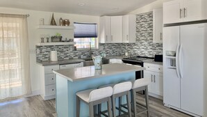 Une cuisine moderne avec des meubles blancs, un îlot central bleu et un réfrigérateur blanc.