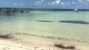 Une plage tropicale aux eaux cristallines, avec une jetée en bois et un bateau visible au loin.