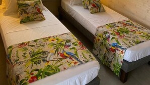 A room with two single beds, each with a floral-patterned bedspread and white pillows. There are two wall-mounted lamps on either side of a window with a view of greenery. - Villa close to all amenities and beach (Saint-François)