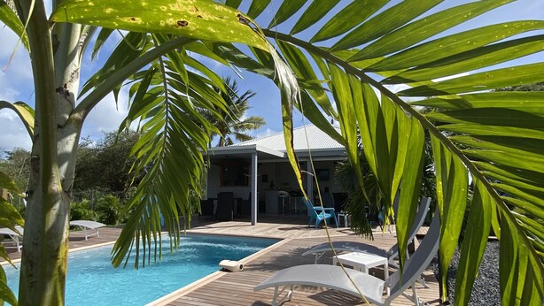 A wooden deck with a pool, lounge chairs, and a building in the background. - Villa close to all amenities and beach (Saint-François)