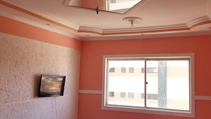 A room with a textured wall, a large window with a view of buildings, and a ceiling with decorative molding. - SEA STIEP APARTMENT (Salvador)