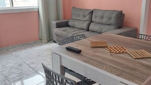 A room with a grey sofa, a wooden table, and a window with curtains. - SEA STIEP APARTMENT (Salvador)