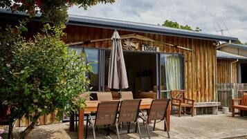 Una cabaña con fachada de madera, un patio con mesa y sillas, y un letrero que dice "Lodge".