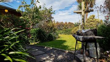 Um jardim com uma cruz de madeira, churrasqueira e um caminho de pedra.