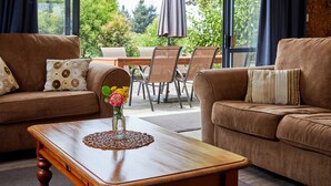 A living room with two brown sofas, a wooden coffee table, and a dining area with a table and chairs. - Barnacle Bills (Kaikoura)