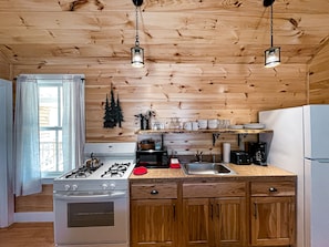 Una cocina con paredes de madera, estufa a gas, pileta y lámparas colgantes.