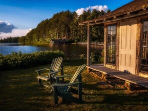 Una cabana al costat del llac amb un moll, dues cadiretes Adirondack i un balcó de fusta.