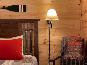 A wooden room with a bed, a lamp, and a chair.