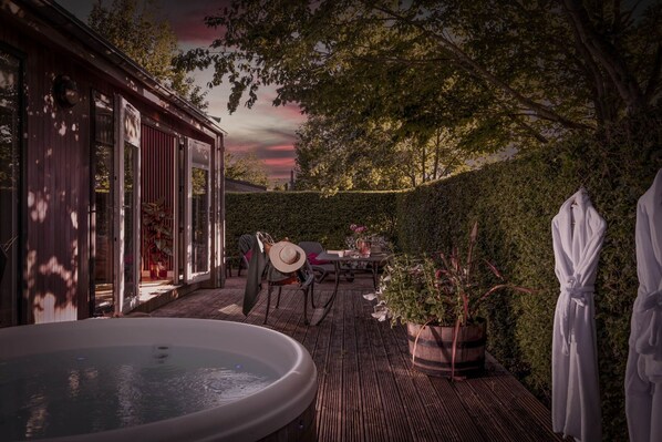 A patio with a hot tub, a table with chairs, and a hedge.