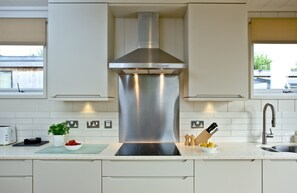 A modern kitchen with stainless steel appliances, a central range hood, and a countertop with a toaster, a bowl of fruit, and a knife block.