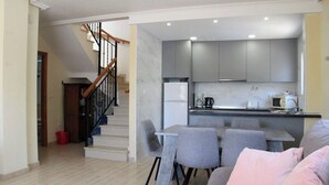 Eine moderne Wohnung mit einer Treppe zum zweiten Stock, einer Küche mit grauen Schränken, einem Essbereich mit grauen Stühlen und einem Wohnzimmer mit einer Couch.