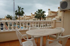 En balkon med et bord og stole, udsigt over en pool og palmer.