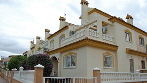 Ein zweistöckiges Gebäude mit beiger Fassade, weißen Balkonen und einem verschlossenen Eingang.