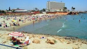 Ein Strand mit einem Hotel im Hintergrund, Sandstrand und badende Menschen.
