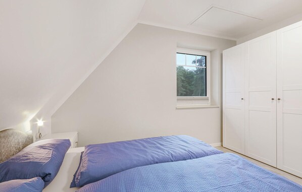 Un dormitorio con techo inclinado, una ventana con vistas a árboles, un armario y una cama con ropa de cama azul.