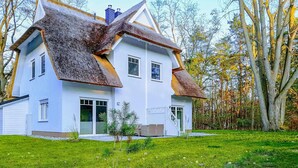 Une maison à deux étages, dotée d’un toit à forte pente, de murs extérieurs blancs et d’un petit porche à l’avant.