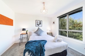 A bedroom with a bed, a window, a hanging light fixture, a side table, and a wall-mounted artwork. - Lake View Greenstone Luxe Apartment (Queenstown)