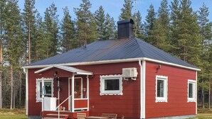 En rød hytte med veranda, skorsten samt et lille bord og bænk.