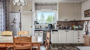 Et kompakt køkken med hvide skabe, et spisebord med stole, et vindue med udsigt til træer og et flisebeklædt bagpanel.