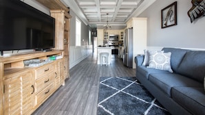 A modern kitchen with wooden cabinetry, a large flat-screen TV, and a central island with bar stools. - Mid City Mansion, Southern Living Walk to streetcar (New Orleans)