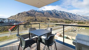 Un balcon avec une table et des chaises, donnant sur un paysage montagneux avec une route et des bâtiments visibles au loin.