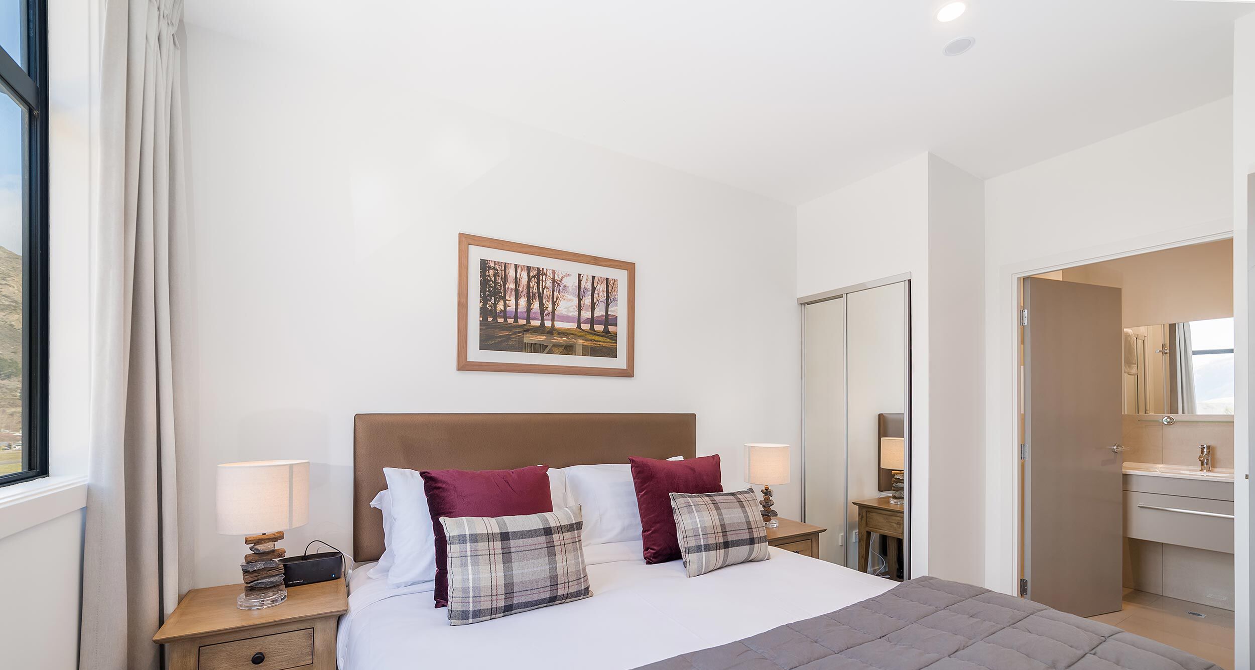 A hotel room with a large bed, a nightstand with a lamp, a mirror, and a painting on the wall.