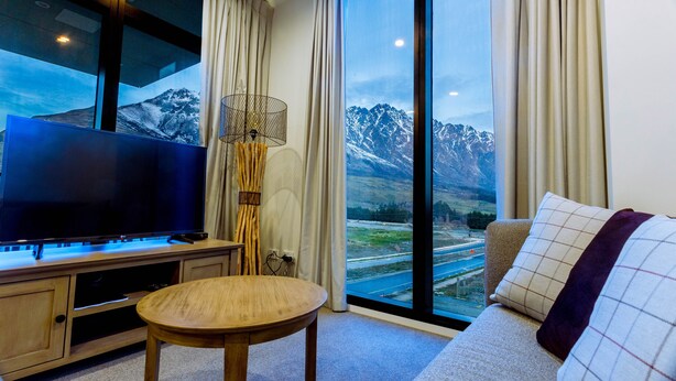 Un salon moderne doté d’un grand téléviseur à écran plat, d’une table basse en bois et d’un canapé offrant une vue sur les montagnes enneigées grâce à de grandes fenêtres.