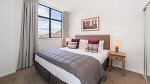 Une chambre à coucher avec un grand lit, une table de chevet avec une lampe, une fenêtre avec des rideaux et un tableau encadré au mur.