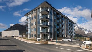 Un immeuble moderne à plusieurs étages, doté de balcons, d’un parking et surplombant un paysage montagneux.