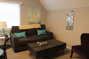 A living room with a dark brown sofa, teal cushions, a coffee table, and a red armchair.