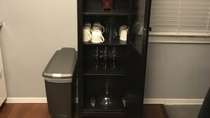 Una cocina con un mueble negro que contiene vajilla, vasos y un reloj.