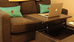 Un sofá marrón con almohadones color turquesa y un ordenador portátil sobre una mesa de madera.