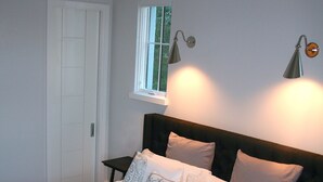 A neatly made bed with patterned pillows, a bedside table, and a window with curtains. - Ion spacious above garage apartment in quiet neighborhood. High ceilings! (Mt Pleasant)