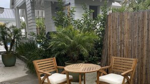 A patio with two wooden chairs and a table, surrounded by potted plants and a wooden fence. - Ion spacious above garage apartment in quiet neighborhood. High ceilings! (Mt Pleasant)