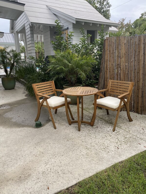 A patio with two wooden chairs and a table, surrounded by potted plants and a wooden fence. - Ion spacious above garage apartment in quiet neighborhood. High ceilings! (Mt Pleasant)