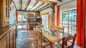 Een rustieke keuken met houten balken, een betegelde vloer en een glazen eettafel met stoelen.