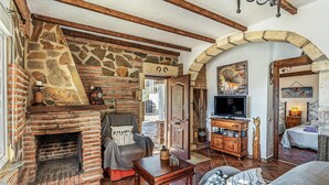 Een gezellige woonkamer met een stenen openhaard, houten balken, een televisie en een comfortabele zithoek.
