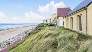 En byggnad som ligger vid kusten och har ett rött tak, intill en sandstrand och havet.