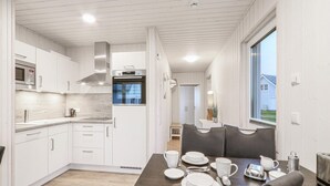 Una cocina moderna con armarios blancos, electrodomésticos de acero inoxidable y un comedor con una mesa dispuesta para cuatro.