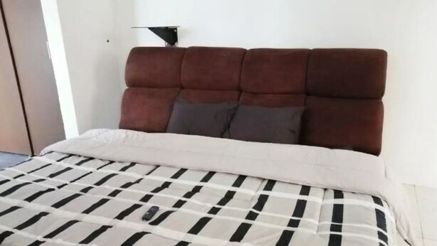 En säng med ett rutigt överkast, en brun klädd sänggavel och två kuddar.