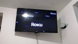 En platt-TV monterad på en vit vägg, som visar Roku-logotypen.