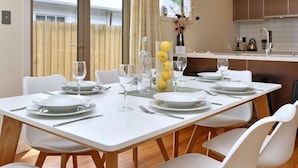 Un coin repas avec une table blanche dressée pour six personnes, comprenant assiettes, couverts et verres.