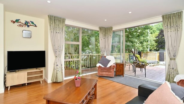 Un salon spacieux doté d’un téléviseur à écran plat, d’une table basse en bois et d’un canapé. Il y a également un balcon avec une terrasse en bois et une chaise.