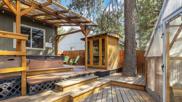 Een houten terras met een pergola, een jacuzzi en een klein houten bouwwerk.