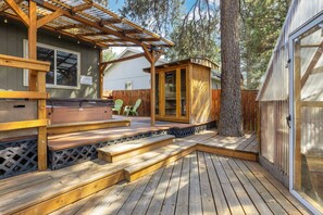 Een houten terras met een pergola, een jacuzzi en een klein houten bouwwerk.