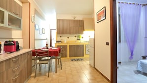 Een compacte keuken met houten kastjes, een eettafel gedekt voor twee personen, en een kleine koelkast.