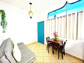 Una habitación con sofá, mesa de comedor, sillas, una puerta azul y cortina.