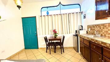 A compact kitchen with a dining area, a teal door, and a window with curtains.