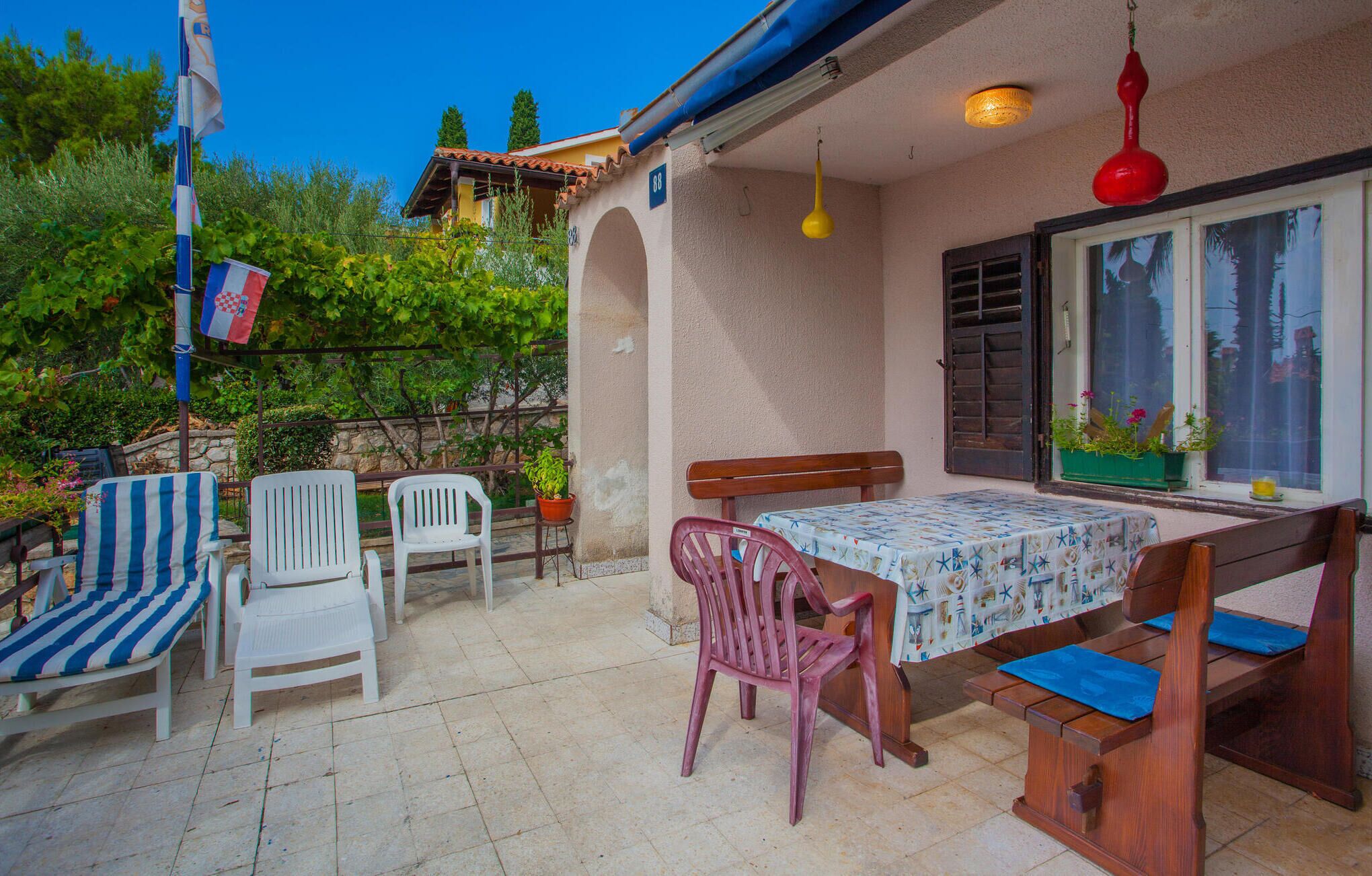 A patio with a table and chairs, a hanging light fixture, and a view of the surrounding greenery.